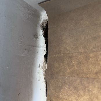 Flawless Results - The image depicts a wall corner with visible damage, including chipped white paint and exposed material underneath. The damage appears to be near the junction of the wall and another surface, possibly indicating wear or structural issues. The background includes a brown surface, likely flooring or a wall covering. - Windows Installation Near Me - Albuquerque, New Mexico