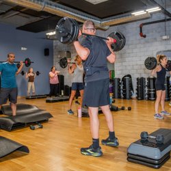 Cornerstone Health & Fitness - Members lift barbells during a group fitness class at our gym in New Hope, featuring polished wood floors, gray brick walls, ...