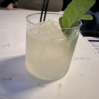 Capri Columbus - Gin & ginseng - A pale-colored cocktail with ice, garnished with a large mint leaf and two black straws, served on a white marble table. - Cocktail Bars Near Me - Columbus, Ohio