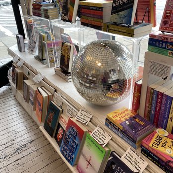 Greedy Reads - Looking outside the window, in the photo you can see books displayed with notes recommending them and a disco ball decoration - Bookstores Near Me - Baltimore, Maryland Greedy Reads - Looking outside the window, in the photo you can see books displayed with notes recommending them and a disco ball decoration - Bookstores Near Me - Baltimore, Maryland