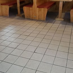 tables and booths - The image depicts a section of a restaurant interior featuring booth seating with wooden dividers and red cushioned seats. The booths are positioned against a wall with a decorative border. The floor is covered with beige square tiles, and the overall setting appears clean and orderly. No people or additional objects are visible in the scene.