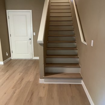 Daniel Ciobanu Constructions - Stairs AFTER - A staircase with wooden treads and a handrail runs along a beige wall in a residential interior, with a white door nearby. - Flooring Near Me