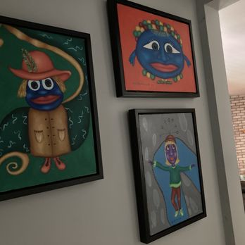 Ultimate Treasures - Three framed paintings featuring abstract, cartoon-like faces and characters are displayed on a gray wall in a living space. - Antiques Near Me - Downers Grove, Illinois