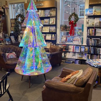 Mitchell's Book Corner - Upstairs at Xmas - A rainbow-lit, holographic Christmas tree with a star topper is displayed inside a bookstore, surrounded by leather chairs, bookshelves, and holiday decorations. - Bookstores Near Me - Nantucket, Massachusetts