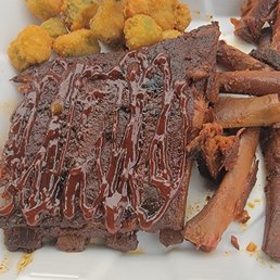Barbecue ribs with sauce, fried okra, and baked sweet potato fries served on a white plate, typical of a country-style eatery.