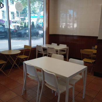 Great Wall - The small dining area with light, bright, and cheerful furniture. - A small dining area with white and yellow tables and chairs, located next to a large window showing the street outside. - Chinese Near Me - Beacon, New York