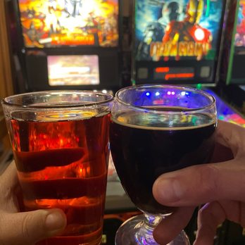 1 Up Arcade Bar - two people holding glasses of beer - Cocktail Bars Near Me - Farmington, Michigan 1 Up Arcade Bar - two people holding glasses of beer - Cocktail Bars Near Me - Farmington, Michigan