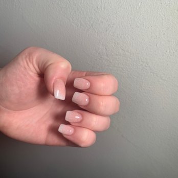 Bliss Nails - Nails - A person's hand with neatly manicured nails painted in a light, glittery pink color is displayed against a plain, textured wall. - Nail Salons Near Me - Wayzata, Minnesota