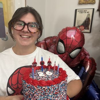 Baked in Nashville - Woman in glasses holding a cake with a Spider-Man ballon behind her. - Desserts Near Me - Nashville, Tennessee Baked in Nashville - Woman in glasses holding a cake with a Spider-Man ballon behind her. - Desserts Near Me - Nashville, Tennessee