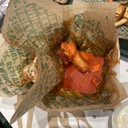 chicken wings in a basket with sauce and french fries