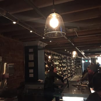 FLG Terroir - Carrie cleans the Reidel in front of the well selected wine wall - Wine Bars Near Me - Flagstaff, Arizona