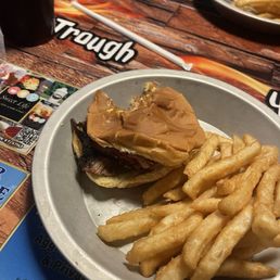 Brisket sandwich and fries. - A metal plate contains a partially eaten peanut butter and jelly sandwich with a side of French fries. The sandwich appears to have peanut butter and jelly spread on bread, with some filling visible. The plate is placed on a restaurant table with a menu, a drink, and a straw nearby. The background shows additional food items and table settings, indicating a casual dining environment.