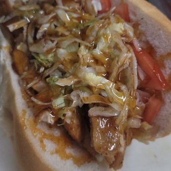 Carmella's Market - The perfect sub for your cheat day - A sandwich with shredded lettuce, tomato slices, and meat inside a bun, topped with sauce, on a white surface. - Cheese Shops Near Me - Boston, Massachusetts