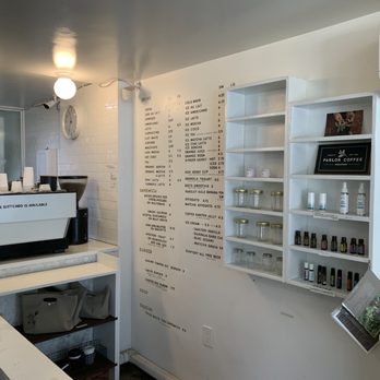 Cafe Cotton Bean - Inside - The image shows the inside of a coffee shop with a white wall, a menu, shelves with jars and bottles, and coffee equipment on the counter. - Coffee & Tea Near Me - Brooklyn, New York
