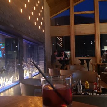 Pivot62 - Fireside - Interior of a bar or restaurant with wooden beams, large windows, and decorative lighting, showing patrons seated at tables. - Pizza Near Me - Vail, Colorado
