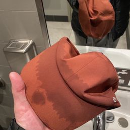 After math of a full body class!! - A hand holds a brown hat with visible water stains in front of a bathroom mirror, with the person's reflection and sink visible.