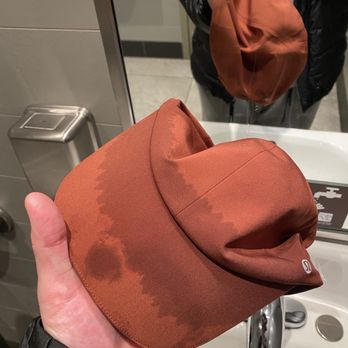 Solidcore - After math of a full body class!! - A hand holds a brown hat with visible water stains in front of a bathroom mirror, with the person's reflection and sink visible. - Pilates Near Me - Watertown, Massachusetts