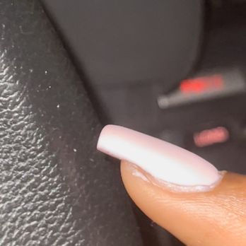 Nails by Reflections - The image shows a finger with a long, white, manicured nail touching a textured black surface, possibly inside a vehicle. - Nail Salons Near Me - Waltham, Massachusetts