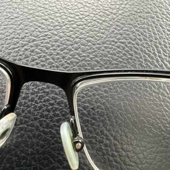 Shopko Optical - Poor fitting lenses. Unacceptable and unprofessional. - A pair of eyeglasses with black frames and clear nose pads is placed on a textured black surface, showing the hinge and part of the lens. - Optometrists Near Me - Bellevue, Wisconsin
