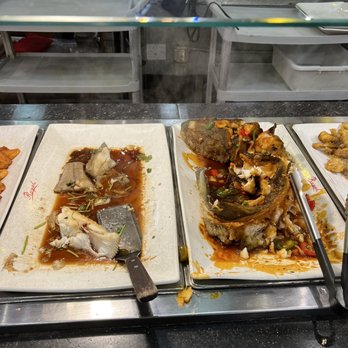 Royal Buffet - Two buffet trays with fish dishes and sauce are shown at an Asian restaurant, with plates, utensils, and kitchen items in the background. - Buffets Near Me - Hoffman Estates, Illinois