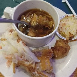 hot and sour soup, baked salmon filet, imitation crab in tin foil, warm imitation cheesy lobster, stuffed shrimp - A plate from Amherst Buffet in Tonawanda, NY, includes a cup of hot and sour soup with vegetables, a foil-wrapped imitation crab, a baked cheesy lobster dish, stuffed shrimp, and a portion of chicken with cabbage. The food is arranged on a white plate with a blue table surface visible in the background.