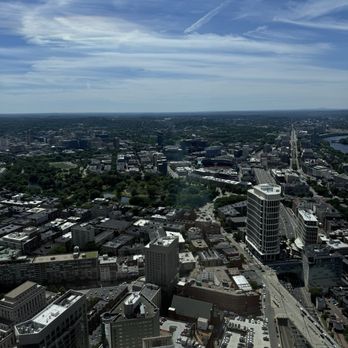 View Boston - An aerial photograph of a city shows tall buildings, green parks, and a river, with a partly cloudy sky overhead. - Observatories Near Me - Boston, Massachusetts