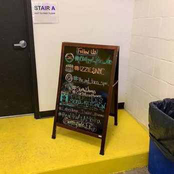 Sunnyside Eats - Instagram - A chalkboard sign with colorful handwritten text and drawings is positioned on a yellow platform against a white wall. The sign lists social media handles and hashtags, including #PlatedLaces_NYC and #IZZIESNYC, and features decorative elements like small illustrations. To the left, there is a black door with a silver handle and a sign indicating 'STAIR A' with an exit direction. The setting appears to be indoors, possibly in a commercial or restaurant space. - Food Delivery Services Near Me - Sunnyside, New York