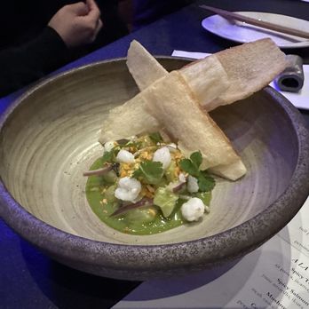 Nohri - Halibut Ceviche - A ceramic bowl contains halibut ceviche garnished with herbs, served with crispy bread slices on a dark table at a restaurant. - Sushi Bars Near Me - Boston, Massachusetts