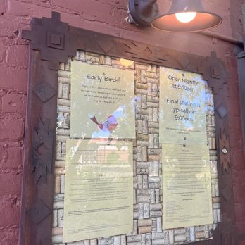 Desert Bistro - A notice board with event information is mounted on a pink brick wall, illuminated by a wall-mounted lamp, with reflections visible on the glass. - New American Near Me - Moab, Utah