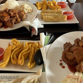 Spa Light - General tso chicken with white rice, crab Rangoon, veggie rolls. - Two plates of Asian-inspired fried foods are displayed on a wooden table. The first plate contains fried chicken with white rice, coleslaw, and a small portion of sauce. The second plate features egg rolls, spring rolls, and small cups of red dipping sauce. The dishes are arranged with utensils and napkins, and the food appears freshly prepared. - Massage Near Me - Lincoln, Rhode Island