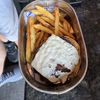 Topgolf - Kids meal hamburger and fries - A metal tray contains French fries and a cheeseburger topped with melted cheese, placed on a dark table. - Sports Bars Near Me - Glendale, Arizona