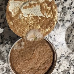 a person dipping batter into a bowl - A round metal can of peanut butter with the lid partially peeled back, revealing the smooth, light brown peanut butter inside. The can is positioned on a speckled granite countertop, with some of the peanut butter visible on the lid and around the opening. The image captures the texture and color of the peanut butter clearly.