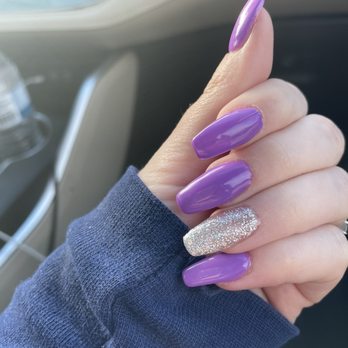 Rosy Nails - Full set - A person's hand with long, purple, glossy nails and one glittery accent nail is visible inside a vehicle, wearing a dark blue sleeve. - Nail Salons Near Me - Hanover, Maryland