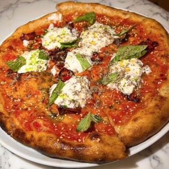 Daphne - A close-up of a pizza featuring dollops of cheese, fresh basil leaves, sesame seeds, and tomato sauce on a golden-brown crust. The pizza is placed on a white plate on a marble table surface, highlighting the toppings and crust details. - Seafood Near Me - Toronto, Ontario