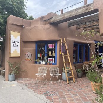 Luna and Luz - Luna Luz boutique in Albuquerque features adobe-style walls, blue window frames, and outdoor seating with potted plants and a wooden ladder. - Jewelry Near Me - Albuquerque, New Mexico