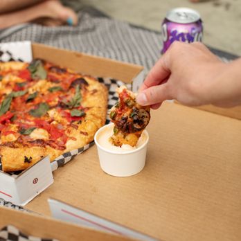 Pizzamoto - a person taking a slice of pizza from a box - Pizza Near Me - Tofino, British Columbia