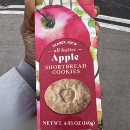 These were good - A person holds a Trader Joe's apple shortbread cookies package with a red apple design, outdoors on a street.