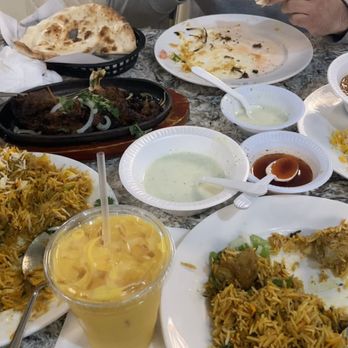 Dera - A variety of Indian and Pakistani cuisine dishes are displayed on a table, including rice, naan bread, curries, and side dishes, with some drinks and condiments. - Pakistani Near Me - Springfield, Virginia