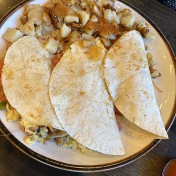 Fame Good Eats - Breakfast tacos with chorizo - A plate contains three breakfast tacos with soft flour tortillas, filled with ingredients such as eggs and chorizo. The plate also has a portion of diced, cooked potatoes. The dish is presented on a dark wooden table, with part of a person's clothing visible in the background. - Breakfast & Brunch Near Me - Morrisville, Pennsylvania