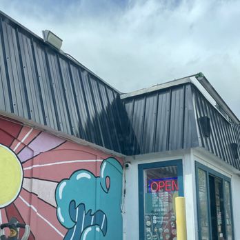 Wave Drinks - Drive thru painted wall - The image shows the exterior of a building with a mural featuring a sun and abstract shapes, along with a neon 'OPEN' sign in the window. - Desserts Near Me - Grand Junction, Colorado