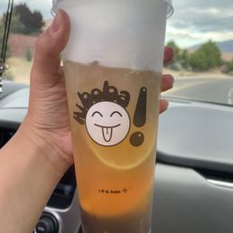 Hawaii Fruit Tea - A person holds a large plastic cup of bubble tea with a cartoon face and exclamation mark on the cup, inside a vehicle.