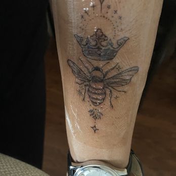 Blacksoul Ink - A tattoo featuring a bee, a crown, and celestial symbols is inked on a person's forearm, with a watch on the wrist. - Tattoo Near Me - North Aurora, Illinois