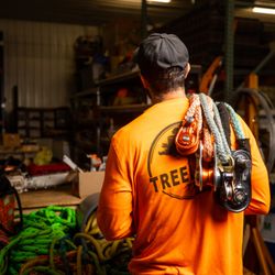 Tree Labs Tree Service - Shaun (owner) in the shop holding rigging slings over his shoulder, in front of table holding ropes