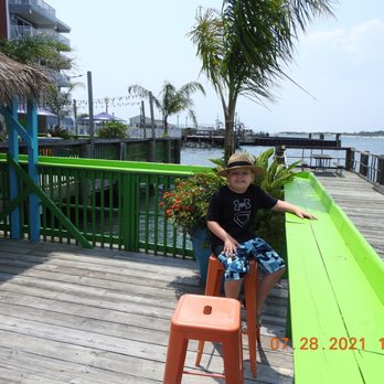 Oc Frog - a young boy sitting on a chair on a dock - New American Near Me - Ocean City, Maryland