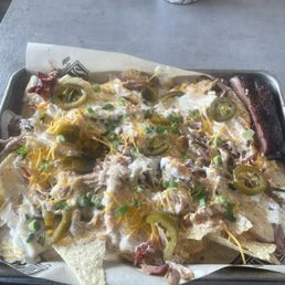 Pulled pork nachos and one rib - A tray of pulled pork nachos with melted cheese, sliced jalapeños, and chopped green onions, served on a metal tray at a restaurant.