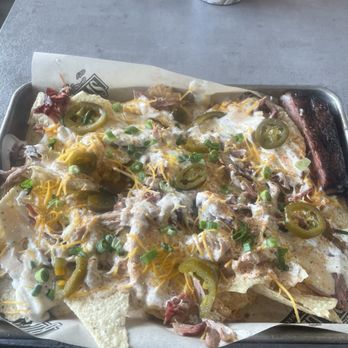 Billy Sims BBQ - Pulled pork nachos and one rib - A tray of pulled pork nachos with melted cheese, sliced jalapeños, and chopped green onions, served on a metal tray at a restaurant. - Barbeque Near Me - Junction City, Kansas