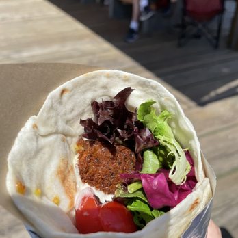 Sprig - a hand holding a burrito with lettuce, tomato, and meat - Greek Near Me - Vancouver, British Columbia Sprig - a hand holding a burrito with lettuce, tomato, and meat - Greek Near Me - Vancouver, British Columbia