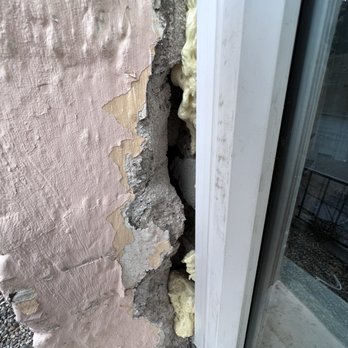 Flawless Results - The image shows a section of a wall with peeling pink paint, revealing underlying concrete and insulation foam. The insulation foam is yellowish and appears to be in the process of installation or repair. The wall is adjacent to a white window frame with a glass pane, and the area suggests ongoing renovation or maintenance work. - Windows Installation Near Me - Albuquerque, New Mexico