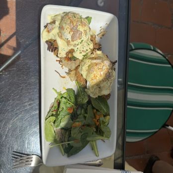 Coronet Cafe - Brisket eggs Benedict - Two eggs Benedict with hollandaise sauce and meat are served on a rectangular white plate, accompanied by a side salad with mixed greens. - Cafes Near Me - Tucson, Arizona