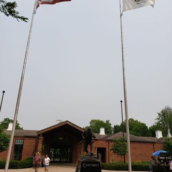 Cantigny - Entrance to visitor center - The image shows the entrance to Cantigny Park's visitor center, featuring a statue, two flags, and a brick building in the background. - Museums Near Me - Wheaton, Illinois